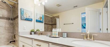 A bathroom with two sinks, a shower, and a large mirror. There are decorative wall art pieces and a towel rack.