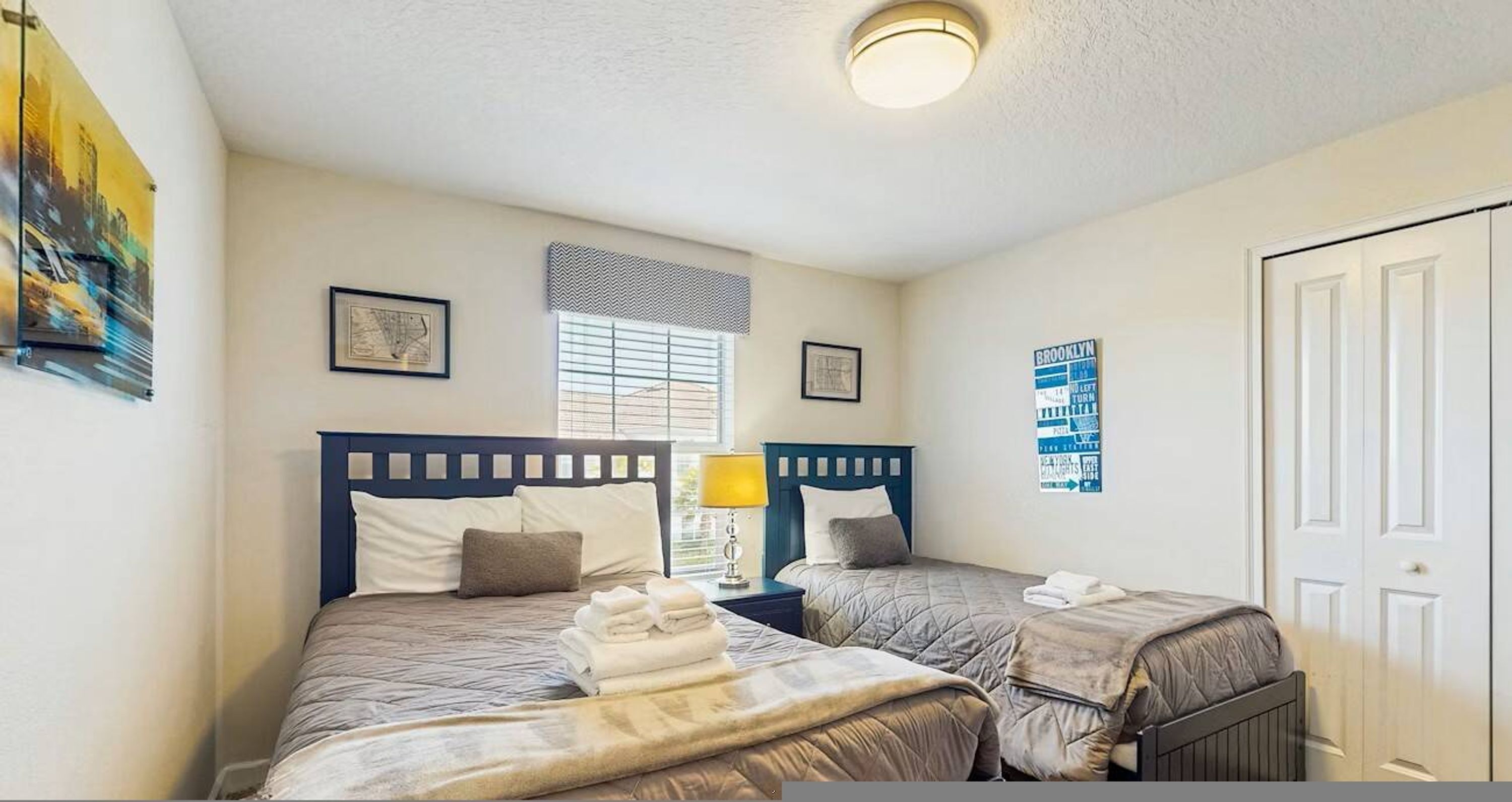 A hotel room with two beds, a window with blinds, a wall clock, and a door.