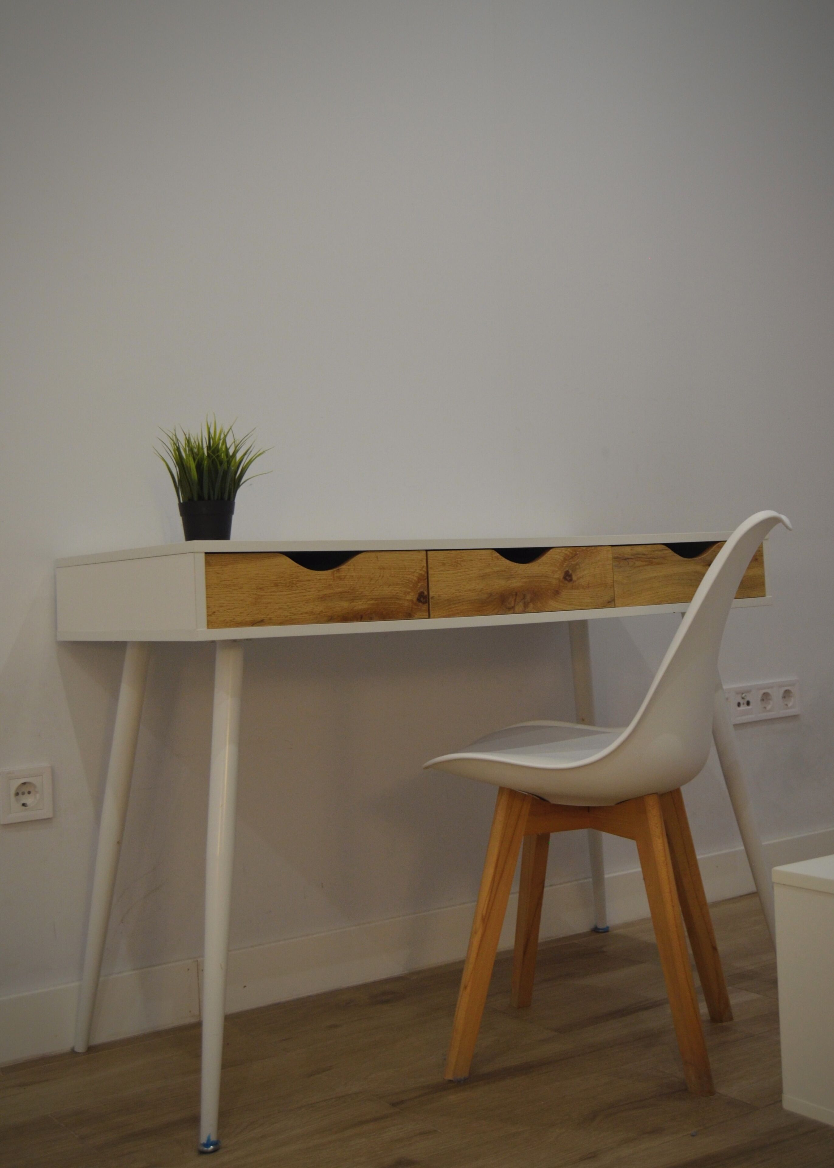 Ein weißer Schreibtisch mit einer Holzplatte und ein weißer Stuhl mit Holzbeinen.