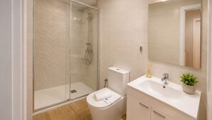 A modern bathroom with a glass-enclosed shower, a white toilet, a sink with a mirror, and a small plant on the countertop.