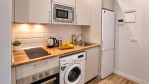 A compact kitchen with a microwave, oven, washing machine, and a refrigerator.