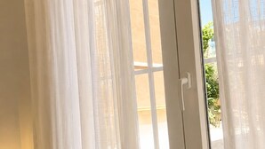 A room with a large glass door, white curtains, and a small potted plant on a shelf.
