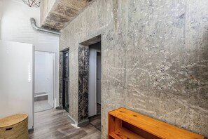 Un pasillo con pared de concreto, un banco de madera y una cesta tejida.