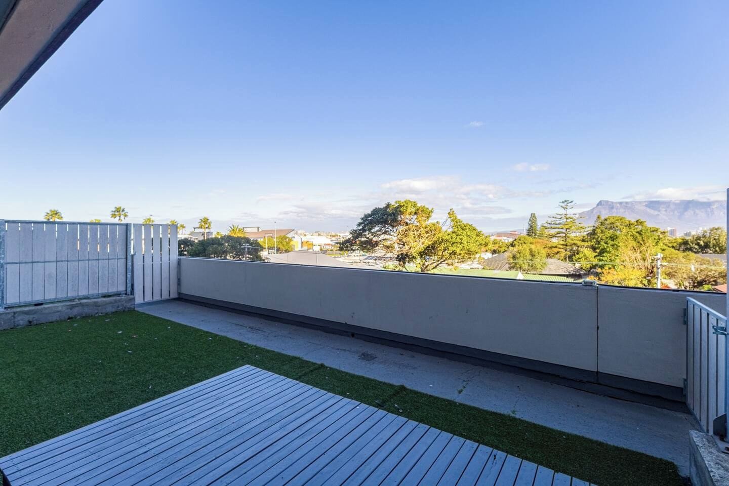 A rooftop patio with a wooden deck, a grassy area, and a view of a cityscape and mountains.