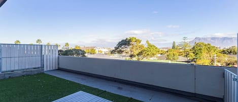A rooftop patio with a wooden deck, a grassy area, and a view of a cityscape and mountains.