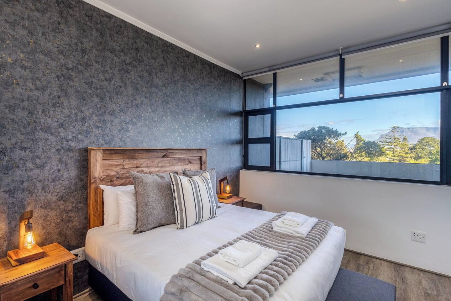 Een moderne slaapkamer met een groot bed, een houten hoofdbord en uitzicht op een berglandschap door een groot raam.
