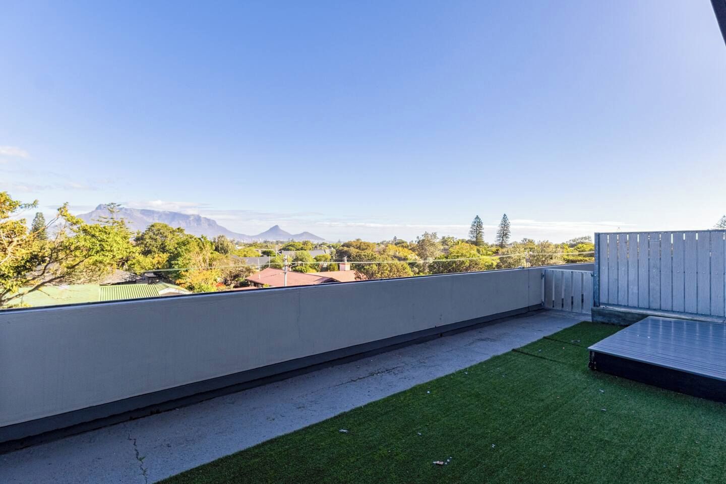 A rooftop terrace with a view of distant mountains, a grassy area, and a wooden fence.