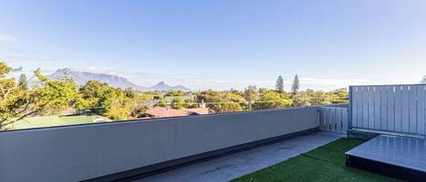 A rooftop terrace with a view of distant mountains, a grassy area, and a wooden fence.
