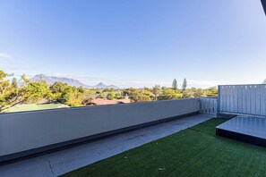Una terraza en la azotea con vistas a montañas lejanas, un área con césped y una cerca de madera.