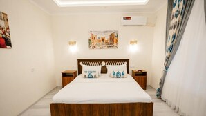 Un dormitorio con una cama de madera, dos mesitas de noche, aire acondicionado de pared y un cuadro sobre la cama.