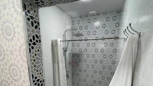 Un baño con azulejos estampados, cabina de ducha de vidrio y un inodoro blanco.
