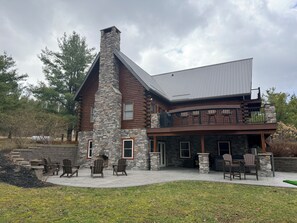 A log cabin with a stone chimney, a balcony with chairs, and a patio area. - Cedar & Stone: Keuka Lake Retreat w/ Hot Tub & Golf (Hammondsport)