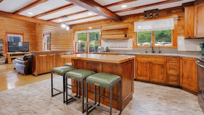 Interior de una cabaña de troncos con cocina, barra y zona de estar.