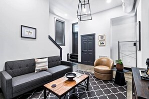 Ein modernes Wohnzimmer mit einem grauen Sofa, einem Holztisch, einem Ledersessel und einem schwarz-weißen Teppich.