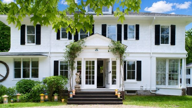 A two-story white house with black shutters, a front porch, and a small garden with lanterns.