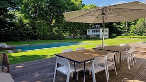 A wooden deck with a pool, a table with chairs, and an umbrella.