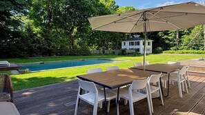Eine Holzterrasse mit Pool, einem Tisch, Stühlen und einem Sonnenschirm.