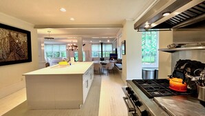 A modern kitchen with a central island, a stove, and a dining area with chairs.