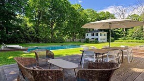 A deck with outdoor furniture, a pool, and a house in the background.
