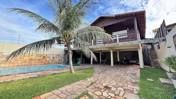 Uma casa com piscina de pedra, uma palmeira e um espaço de varanda coberto.