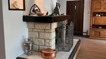 Una chimenea de piedra con una rejilla de metal, una olla de cobre y un jarro de metal sobre un piso de baldosas.