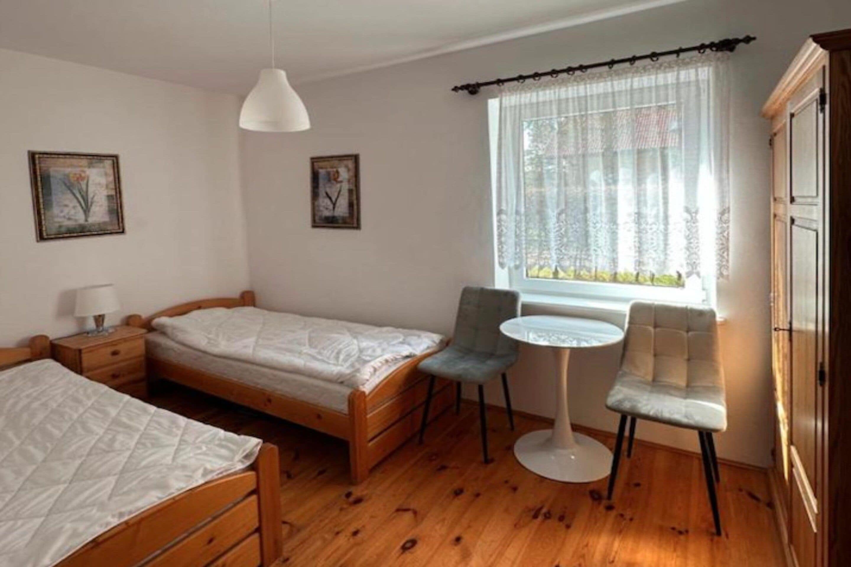 Quarto com duas camas de solteiro, uma mesa pequena, uma cadeira e uma janela com cortinas.