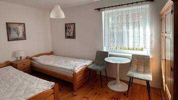 Quarto com duas camas de solteiro, uma mesa pequena, uma cadeira e uma janela com cortinas.