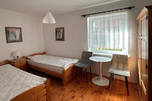 A bedroom with two single beds, a small table, a chair, and a window with curtains. - Large Holiday Villa With Private Garden (Choczewo)