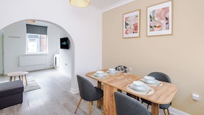 A dining area with a wooden table set for four, two framed artworks on the wall, and a television mounted on the wall.