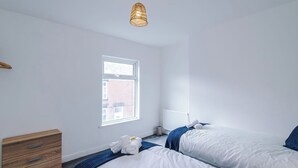 A bedroom with two beds, a wooden dresser, a radiator, and a window.
