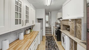 A kitchen with white cabinets, a wooden countertop, a marble backsplash, a washing machine, and a tiled floor. - Elegant 3BR | Short London Commute | Fast Wi-Fi (Greater London)