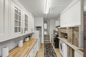 Eine Küche mit weißen Schränken, einer Holz Arbeitsplatte, einer Marmor Spritzschutzleiste, einer Waschmaschine und einem gefliesten Boden.