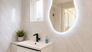 A bathroom with a white vanity, a round mirror with a light, a potted plant, and a rug. - Elegant 3BR | Short London Commute | Fast Wi-Fi (Greater London)