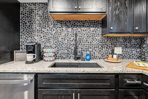 A kitchen with a stone backsplash, a coffee maker, a sink, and dark wooden cabinets.