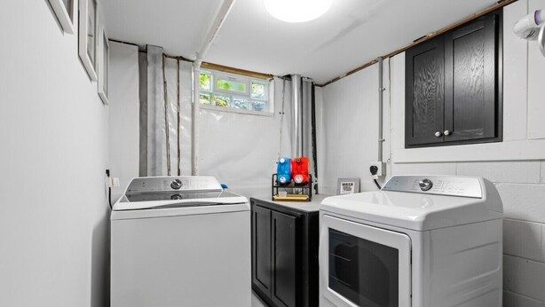 A laundry room with two washing machines, a cabinet, and a window with a view. - Modern Reynoldsburg Retreat Near Columbus (Reynoldsburg)
