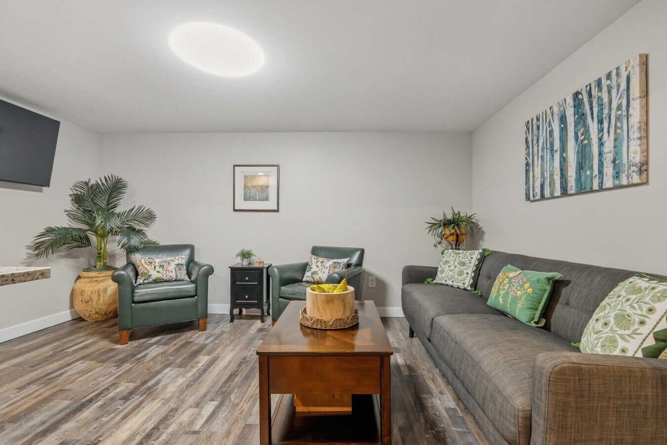 Un salon comprenant un canapé, deux fauteuils, une table basse et un téléviseur fixé au mur.