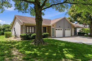 Ein zweistöckiges Haus mit Garage, einem großen Baum im Vorgarten und einem gepflegten Rasen.