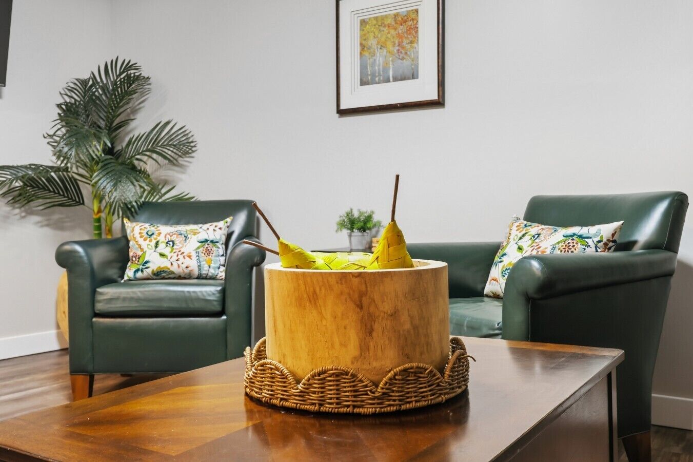Una sala de estar con dos sillones verdes, una mesa de centro de madera y una maceta de madera decorativa con flores amarillas.