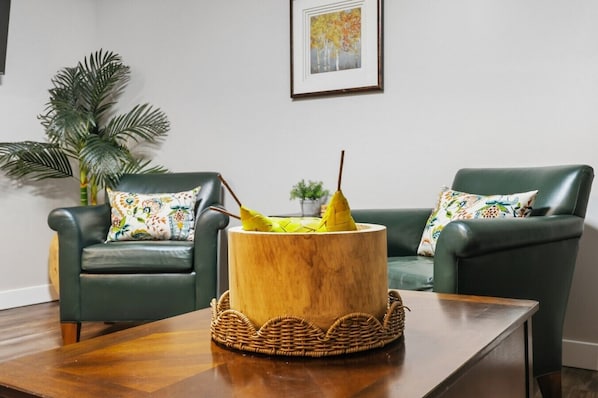 A living room with two green armchairs, a wooden coffee table, and a decorative wooden planter with yellow flowers.