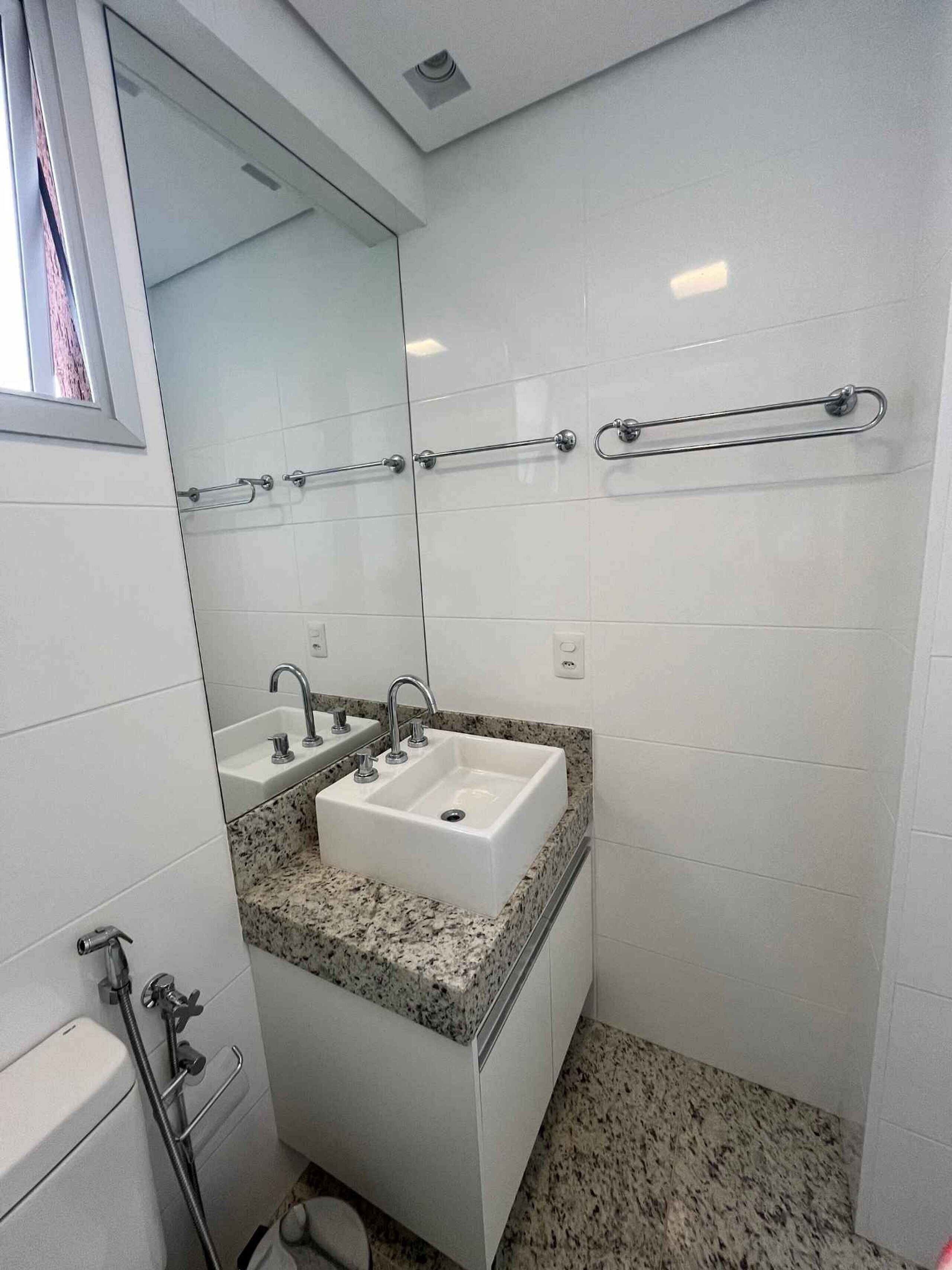 Un baño con un lavabo blanco, dos grifos, un espejo y un perchero para toallas.