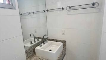 Un baño con un lavabo blanco, dos grifos, un espejo y un perchero para toallas.