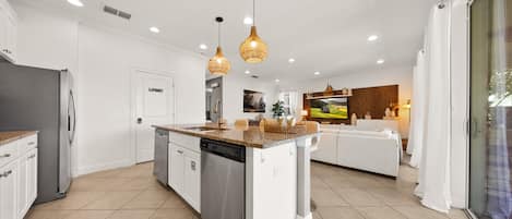Una cocina moderna con una isla central, electrodomésticos de acero inoxidable e iluminación colgante.