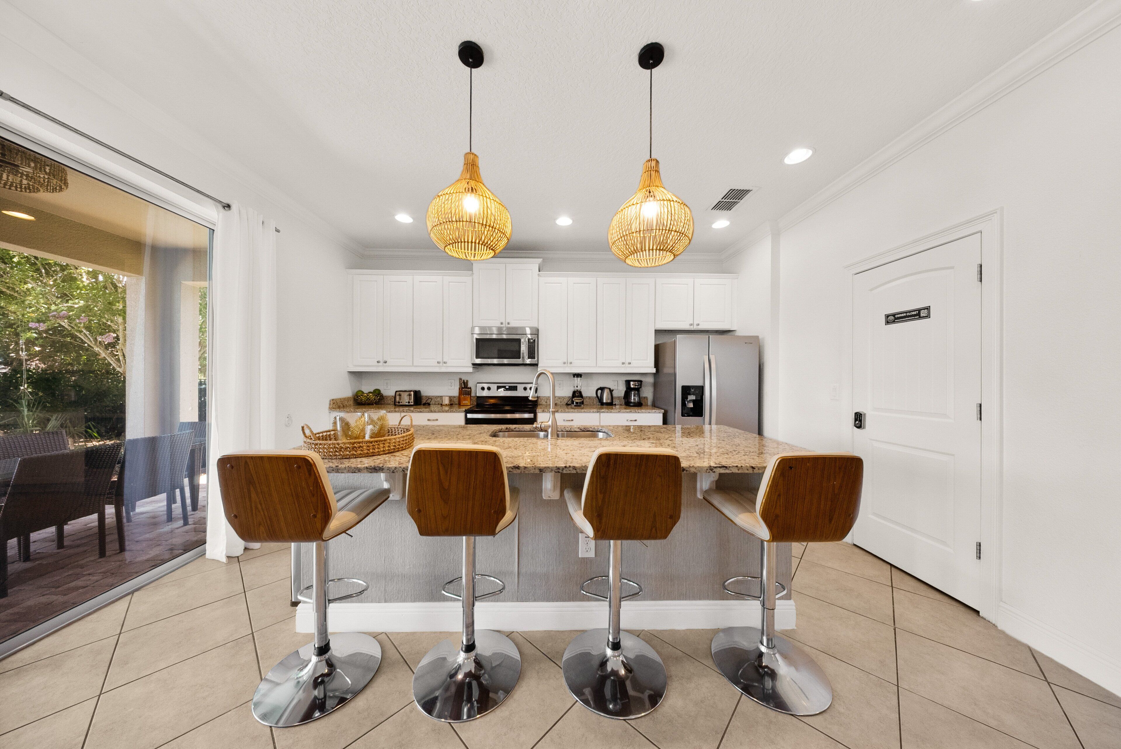 Una cocina moderna con gabinetes blancos, electrodomésticos de acero inoxidable y una isla central con taburetes de bar.