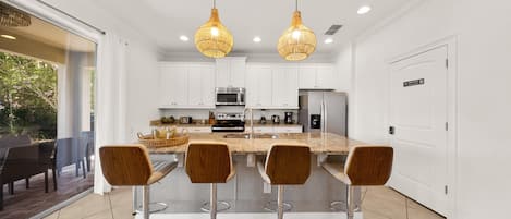 Una cocina moderna con gabinetes blancos, electrodomésticos de acero inoxidable y una isla central con taburetes de bar.