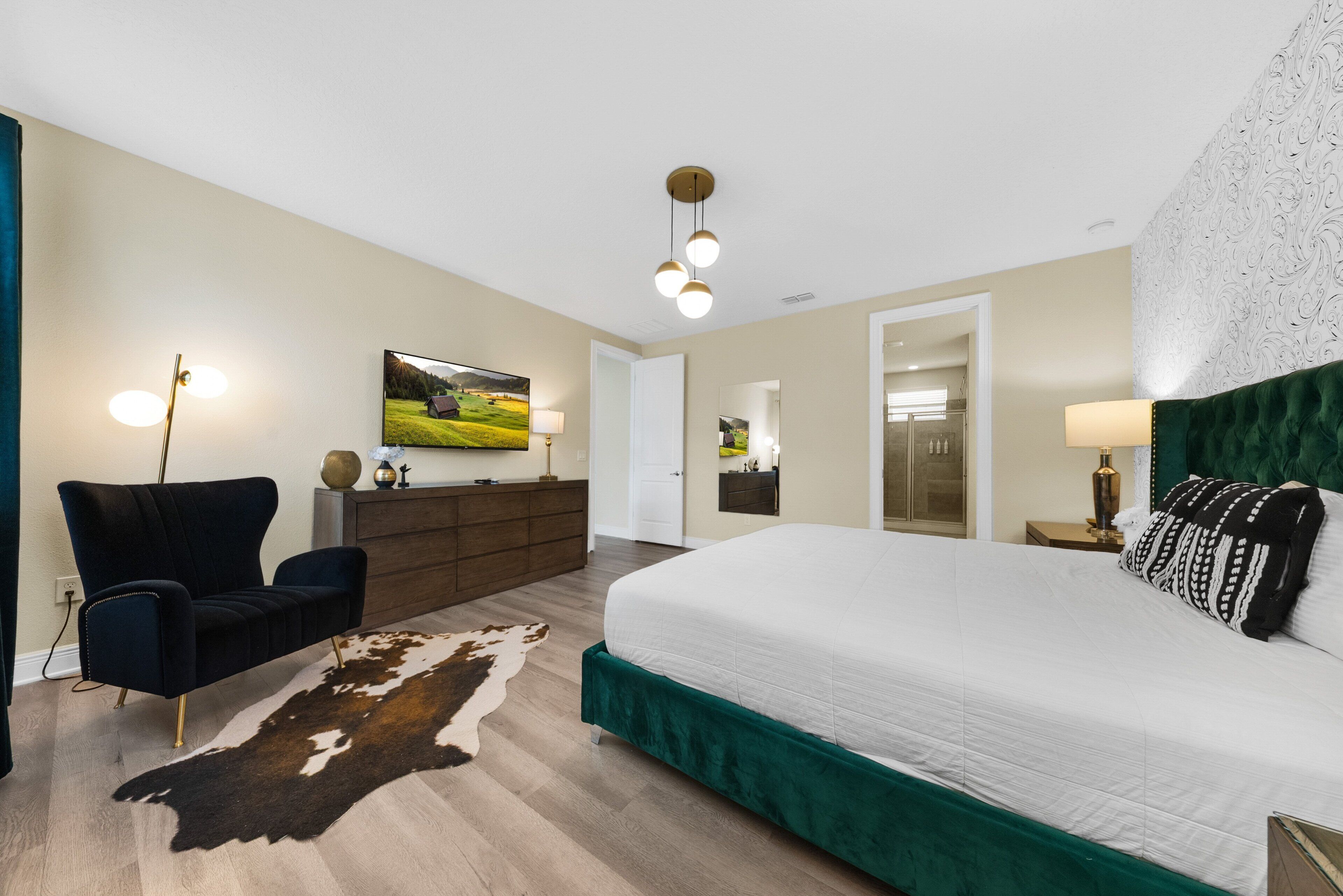 Une chambre à coucher avec un grand lit, un téléviseur fixé au mur, une commode et une chaise.