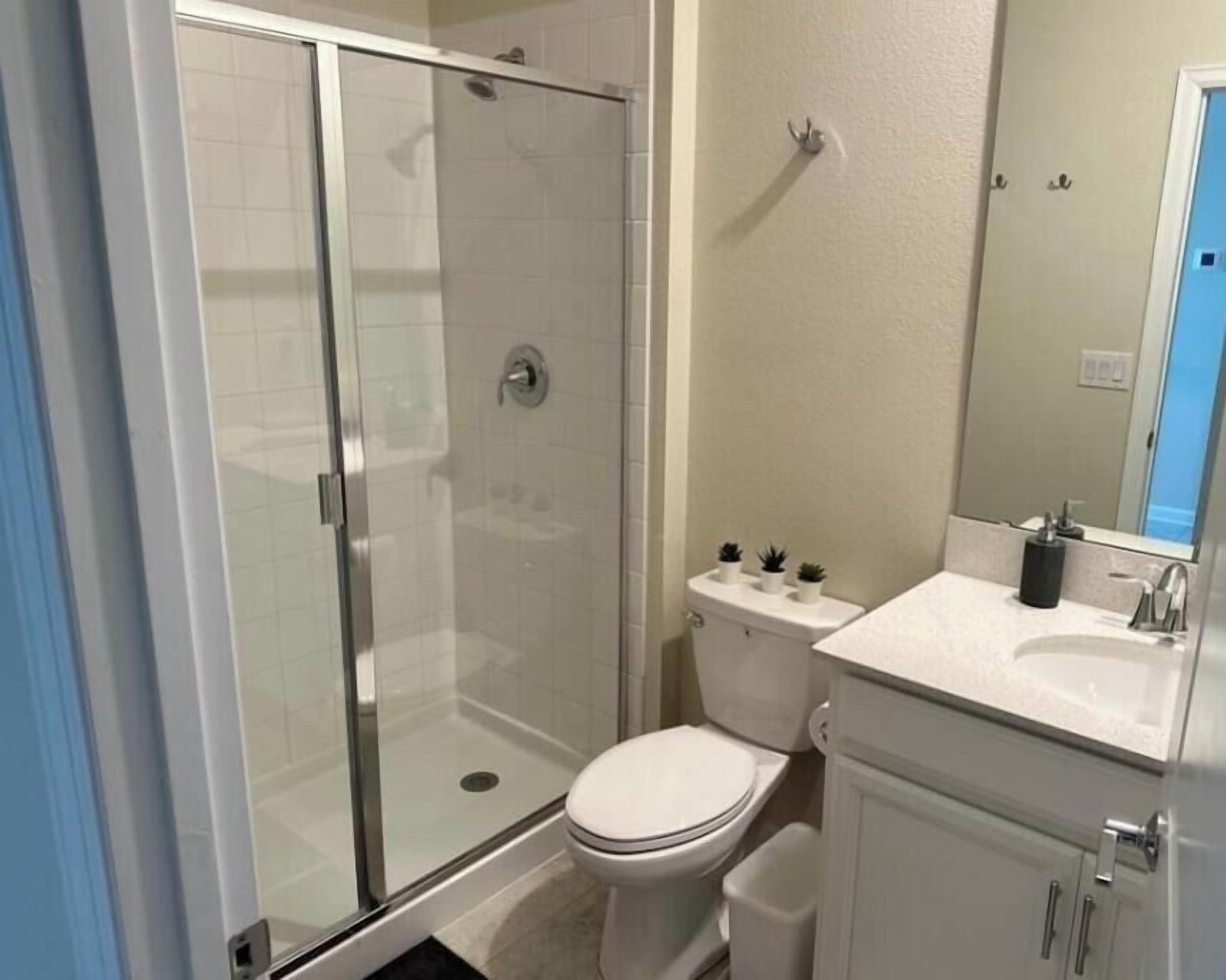 Un baño con cabina de ducha de vidrio, inodoro y lavabo con espejo.