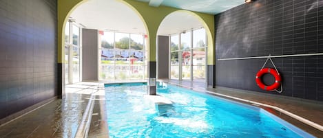 An indoor swimming pool with clear glass walls, a lifebuoy, and a tiled floor.