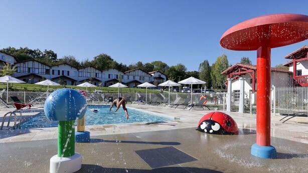 A water park with a pool, water play structures, and umbrellas.