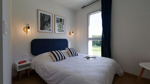 A bedroom with a bed, bedside tables, wall-mounted lights, framed pictures, and a window with curtains.