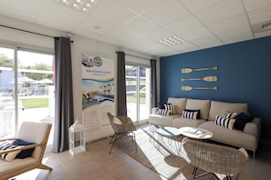 Ein modernes Hotelzimmer mit großem Fenster, einer Couch, einem Sessel, einem kleinen Tisch und einer Wand mit Stand-Up-Paddles.